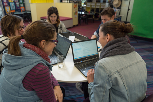 Five teachers sitting around a table planning on laptops